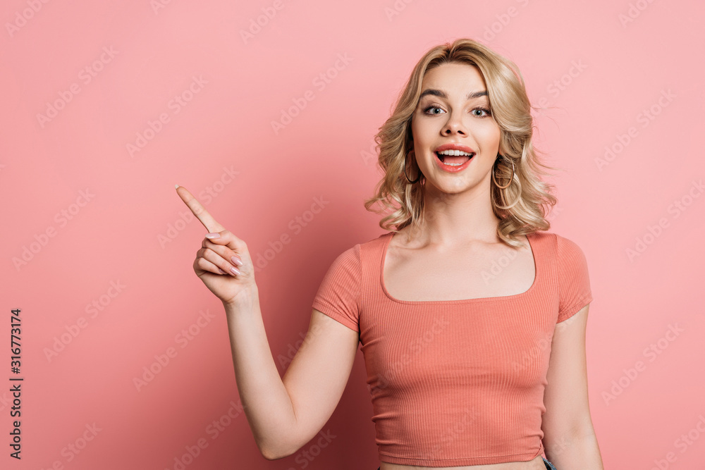 cheerful girl pointing with finger and looking at camera on pink background cheerful girl pointing with finger and looking at camera on pink background