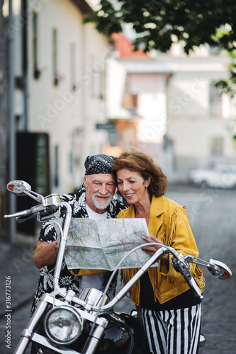 A cheerful senior couple travellers with motorbike in town, using map.