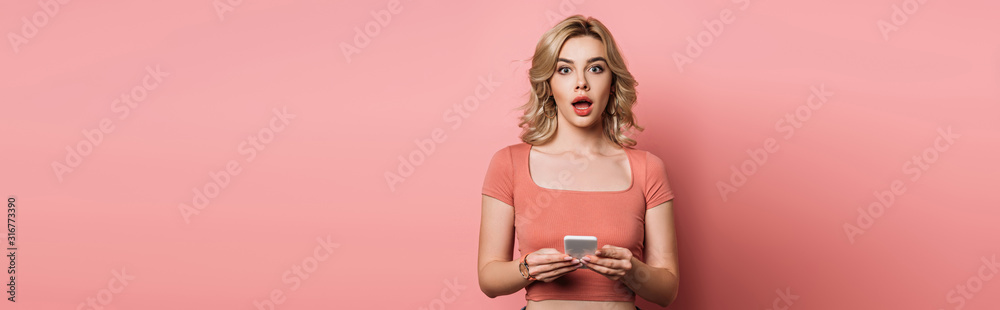 panoramic shot of shocked girl looking at camera while chatting on smartphone on pink background panoramic shot of shocked girl looking at camera while chatting on smartphone on pink background