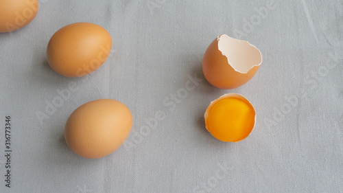 Three chicken brown eggs and one broken egg with yolk in shell on a gray background. Isolated