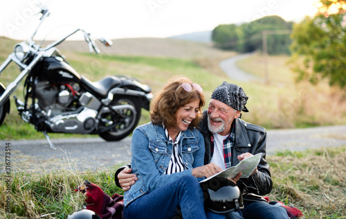 Cheerful senior couple travellers with map and motorbike in countryside.