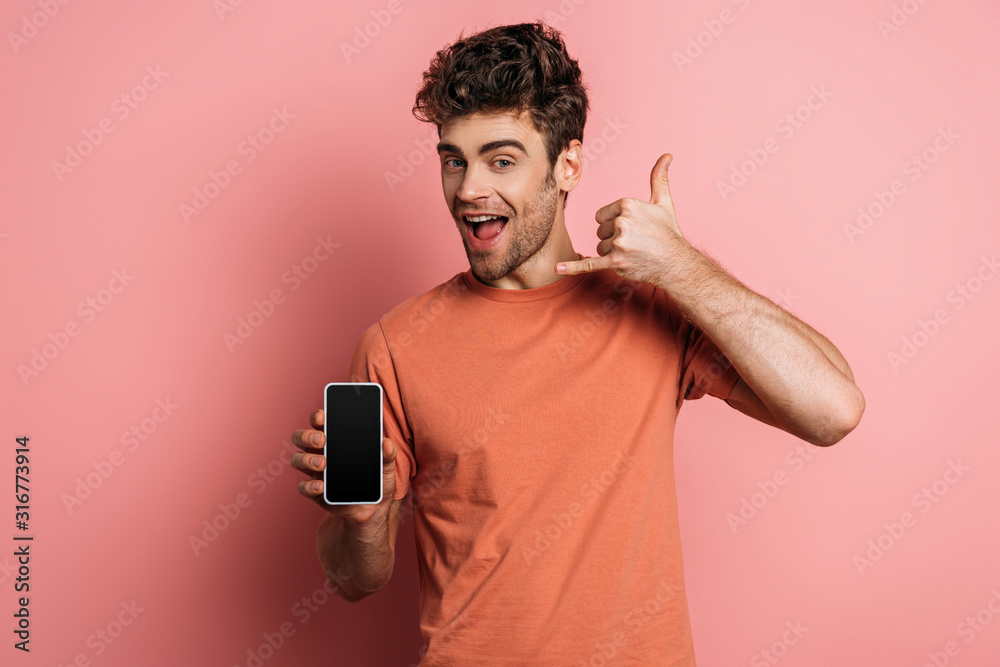 cheerful young man showing lets drink gesture while holding smartphone with blank screen on pink background cheerful young man showing lets drink gesture while holding smartphone with blank screen on pink background