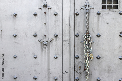 Closeup of old Iron door with closed padlock on a chain. A chain of silver color with closed padlock on an old gate. © Mike Sagan