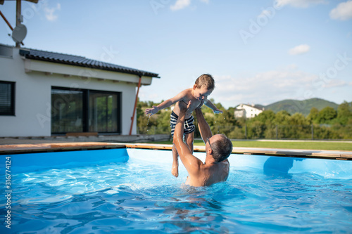 Fotografia A father with small son playing in swimming pool outdoors.