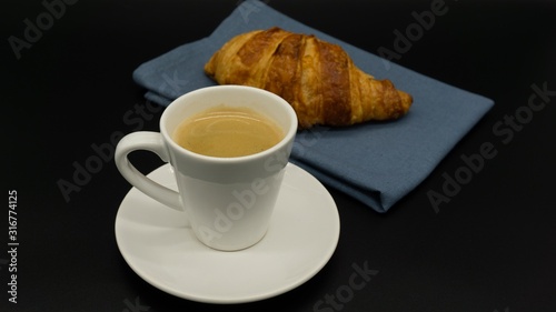 Cup of espresso coffee with a croissant on a blue napkin. Isolated. Black background. 