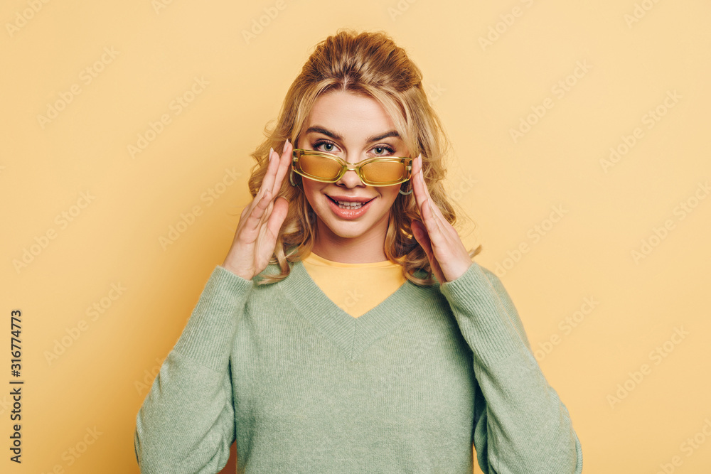 smiling girl touching glasses while looking at camera on yellow background