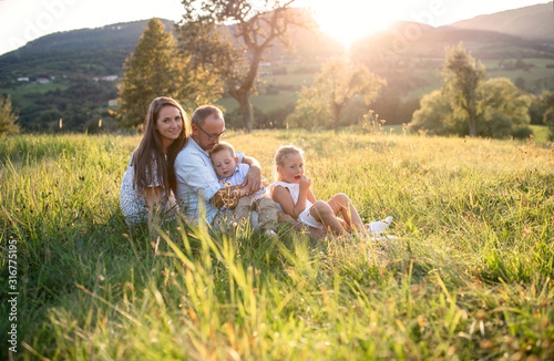 Young family with two small children sitting on meadow outdoors at sunset. © Halfpoint