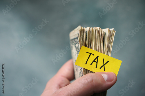 Taxes concept with one dollar bills in a hand and text Tax. photo