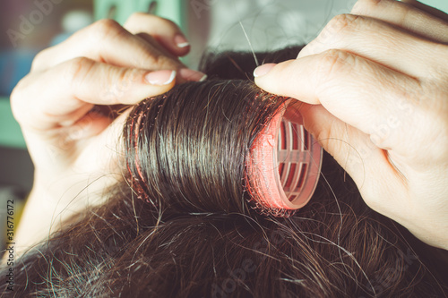 Girls hands curl hair on red curlers.
