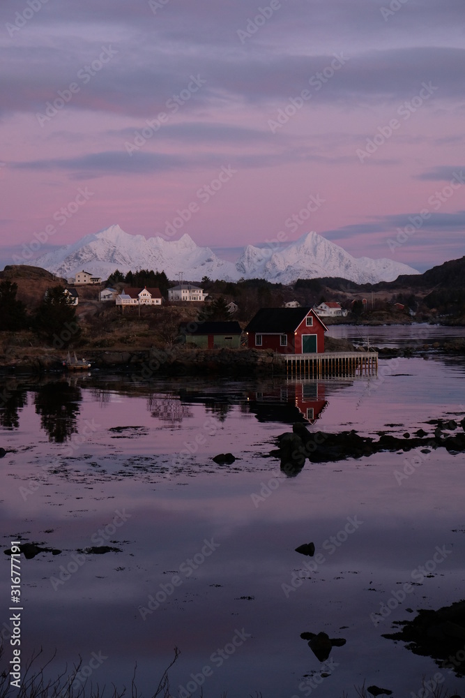 Obraz premium Beautiful typical fishermans town located in Lofoten Islands, Norway. Rorbu houses in the bay of Ballstad. Pink sunrise in the background. 