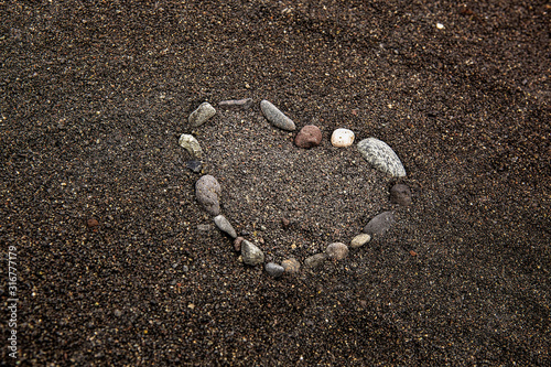 heart laid out of stones on the beach on black sand