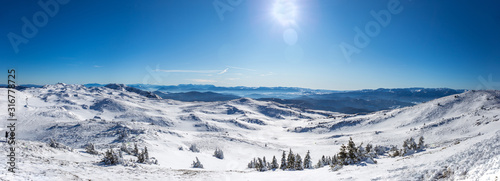 Panoramic shot from the top of the mountain in winter season. Everything is covered in snow and looks beautiful. The day is sunny and the sky is clear and blue.