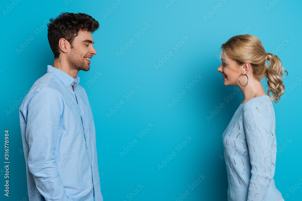 side view of happy man and woman smiling at each other on blue background side view of happy man and woman smiling at each other on blue background