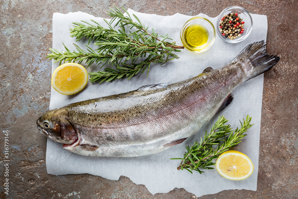Raw trout fish on paper with rosemary and lemon on a stone table, top view Raw trout fish on paper with rosemary and lemon on a stone table, top view