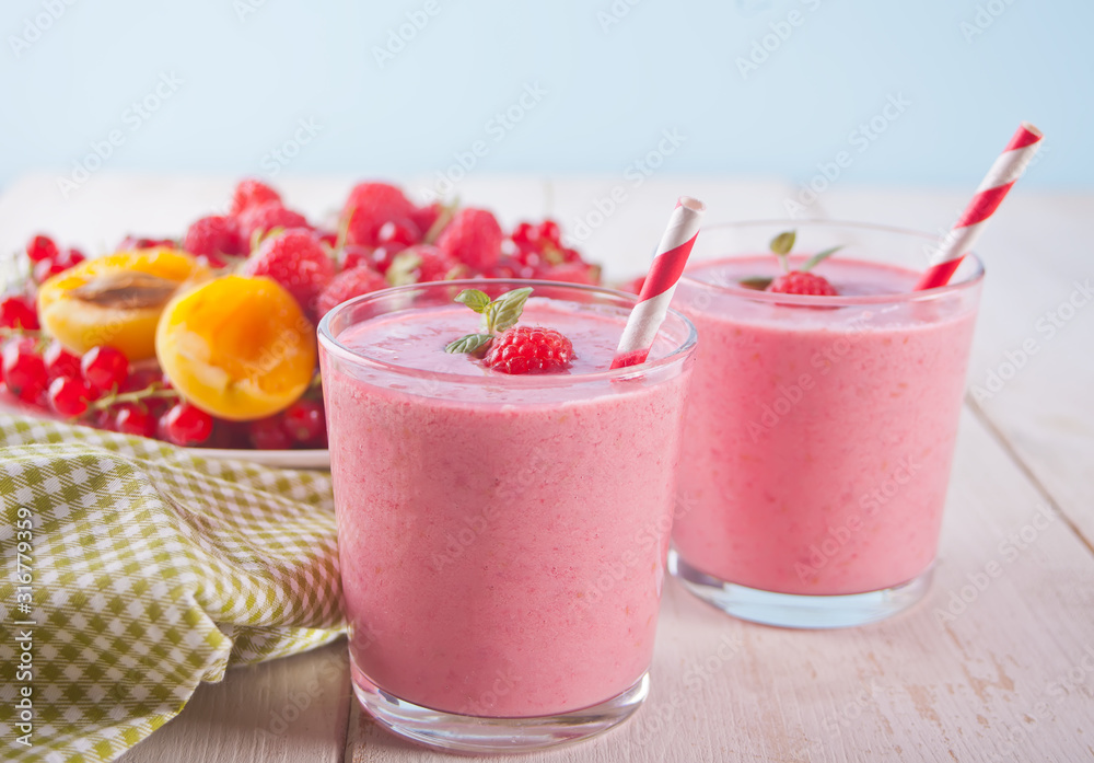 Rwo glass of raspberry smothies with berries on the plate on the white wooden table Rwo glass of raspberry smothies with berries on the plate on the white wooden table