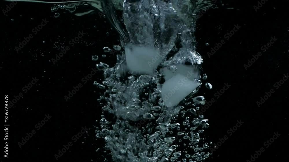 Slow motion ice cubes falling down in water on black background with splash, bubbles and drops