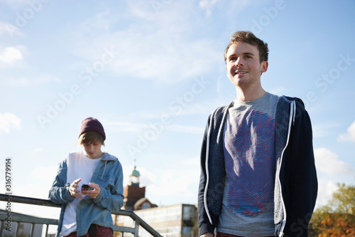 Low angle view of young man using mobile phone with friend in foreground