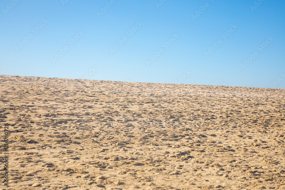 Blue sky over a golden yellow sand dune with a lot of structures and shapes close to a beach where pople enjoy a sunbath and their holiday vacation travel