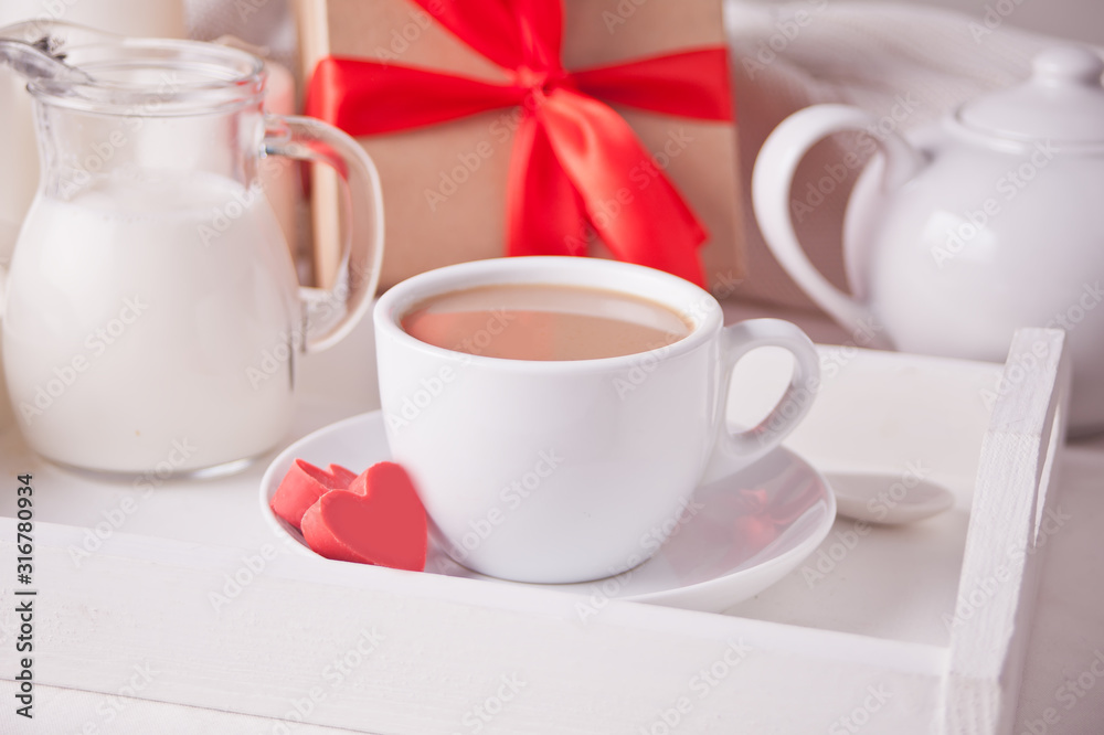 Cup of coffee and a heart shaped red chocolate candies with gift box on the white tray Cup of coffee and a heart shaped red chocolate candies with gift box on the white tray