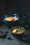 Asian ramen noodles soup with beef, oyster mushrooms and vegetables in bowl on dark background