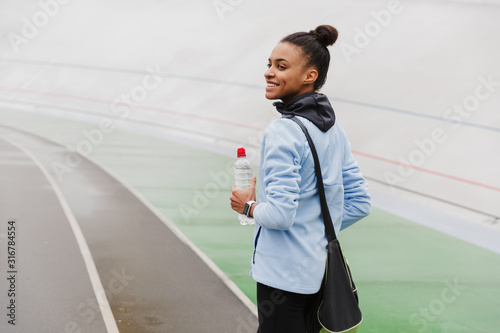 Smiling fit young african sportswoman carrying sportsbag photo