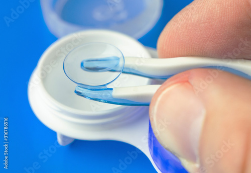 Hand with silicone tweezers takes out a soft contact lens  from the storage container. 