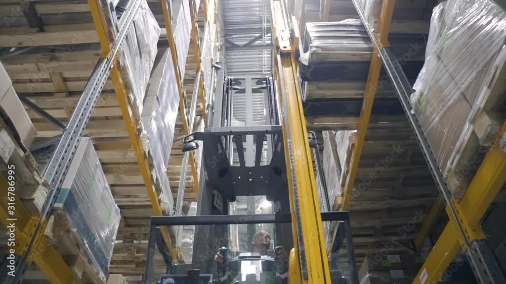 Warehouse male worker with forklift. loader unload goods from shelves. concept logistics, elevator, distribution. driver on car remove take down cargo cardboard box. delivering merchandise. Warehouse male worker with forklift. loader unload goods from shelves. concept logistics, elevator, distribution. driver on car remove take down cargo cardboard box. delivering merchandise.