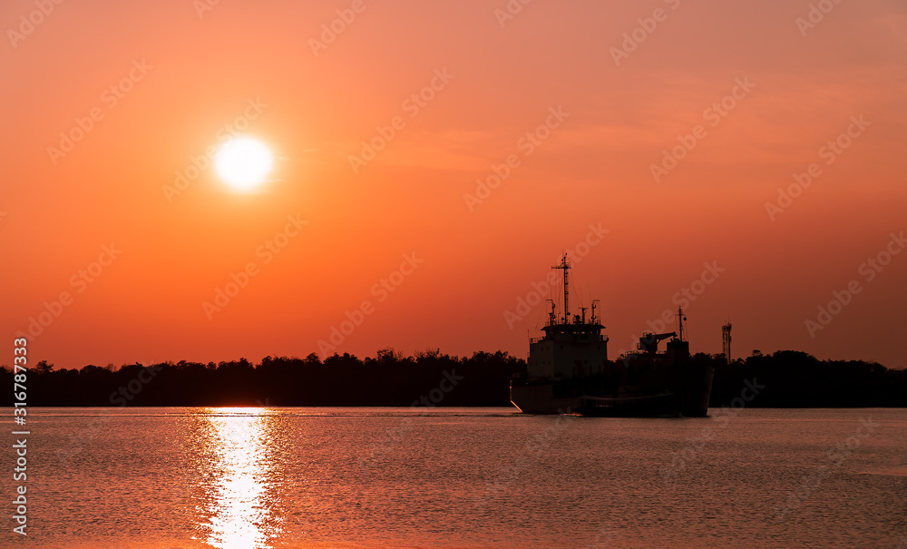 Dark shadow of larger fishing ship floating in the sea. With be hind background was silhouetted the mangrove forest along the coast. During in sunset and dark color the sky.