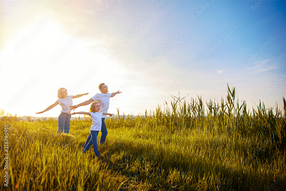 Photo A happy family in white T-shirts, sunglasses and jeans in the park spread apart arms mimicking airplanes. Summer. Vacation air travel concept.