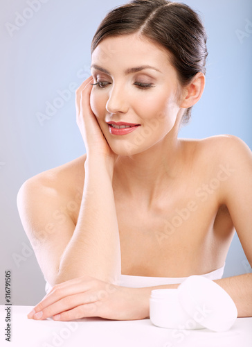 Skin care concept portrait with young woman looking down at cream jar.
