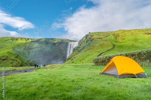 Camping site with tents in front of famous Skogarfoss waterfall  while hiking in Iceland  summer