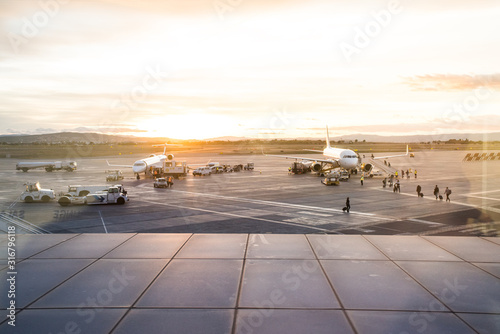 Airplanes on the airport runway. Operators loading and unloading and people boarding the planes. Airport at sunset