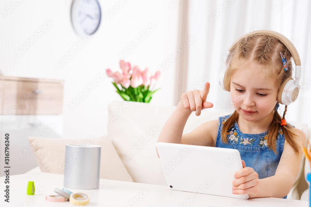 Beatiful kid pointing her finger at tablet, playing some games with headphones on Beatiful kid pointing her finger at tablet, playing some games with headphones on