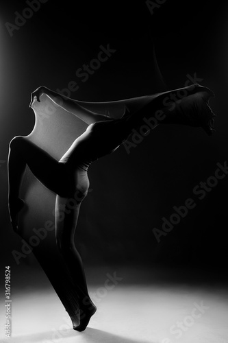 Slim girl wearing a white bodysuit dances a modern avant garde dance, covering her body with elastic transparent fabric. Artistic, conceptual, monochrome and creative design. Silhouette photography.