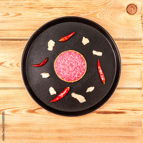 Close-up slice smoked sausage with slices parmesan cheese and red chili pepper on black stone plate
