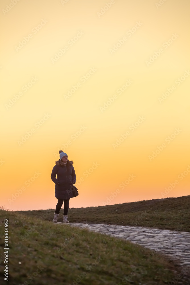 Lady walks in the public park during a beautiful colorful afternoon winter dusk.