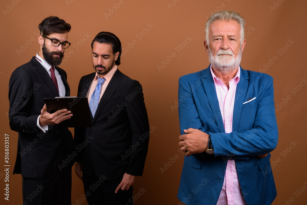 Three multi ethnic bearded businessmen together against brown background Three multi ethnic bearded businessmen together against brown background