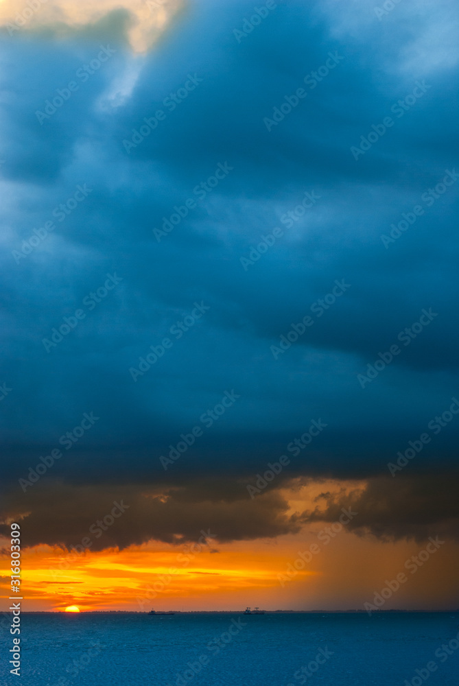 Ships in the sea on a background of clouds with rain during sunset / sunrise. The sun on the horizon. Rain at sea during sunset / sunrise. Contrast blue and yellow