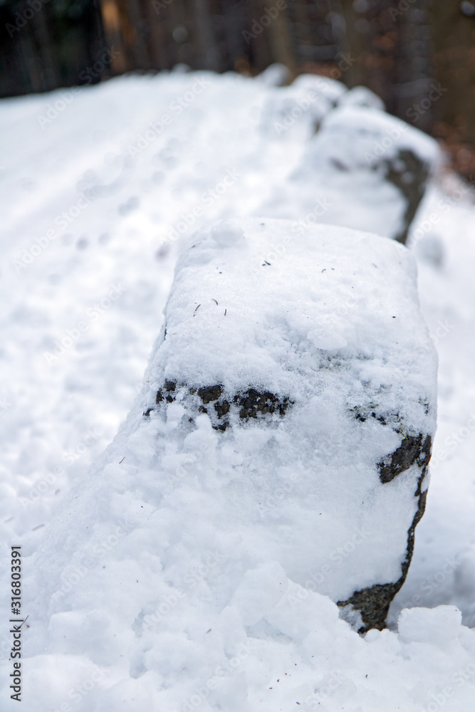 The snowy boundary stone on the mountain road. Aged border stone on the winter way in the mountain.