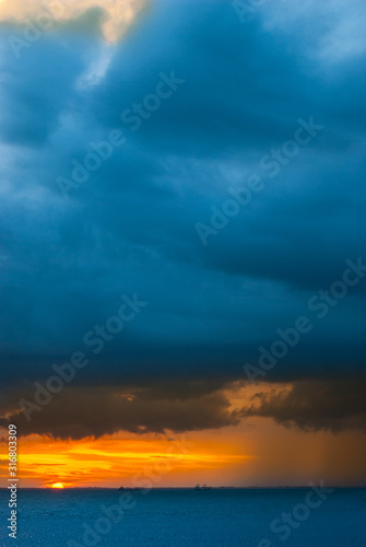 Ships in the sea on a background of clouds with rain during sunset / sunrise. The sun on the horizon. Rain at sea during sunset / sunrise. Contrast blue and yellow
