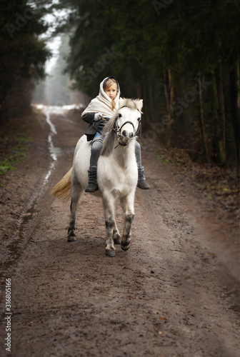 A little village girl in modest clothes walks in the winter with her little white pony in the forest. Original image. Country life. © AlesiaKan