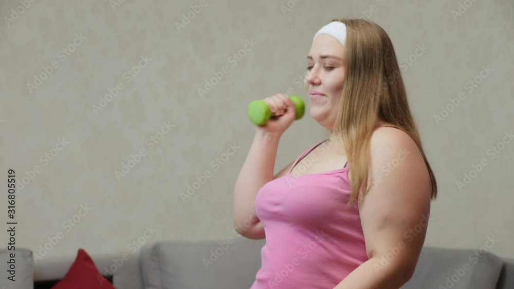 Happy overweight girl dancing and doing exercises with dumbbells in the room, close-up Happy overweight girl dancing and doing exercises with dumbbells in the room, close-up