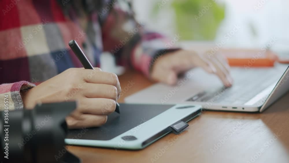 Side view of Asian women designer working on a laptop with graphics tablet Side view of Asian women designer working on a laptop with graphics tablet