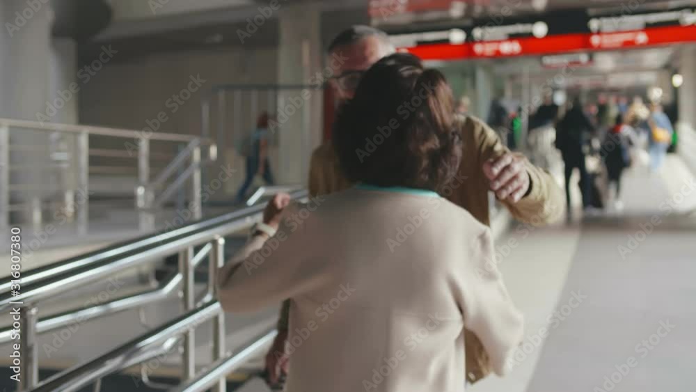Portrait of aged husband and wife hugging at railway station. Woman meeting her husband in airport Portrait of aged husband and wife hugging at railway station. Woman meeting her husband in airport