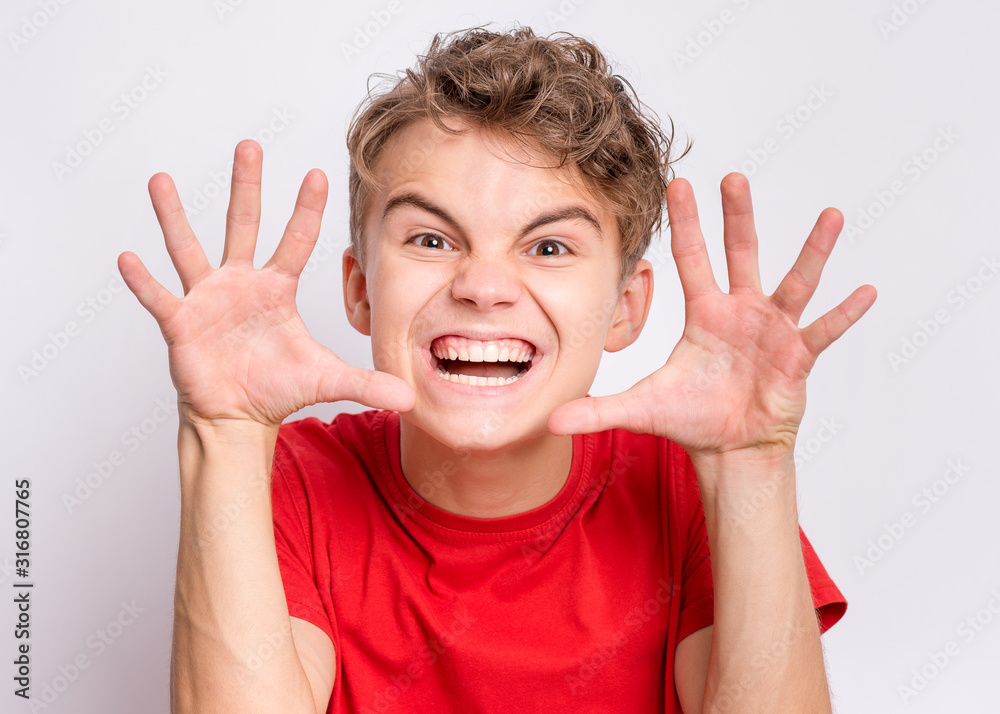 Teen boy trying to frighten someone with stretched hands. Emotional portrait of angry child with hand up on grey background. Negative human emotion, facial expression. Teen boy trying to frighten someone with stretched hands. Emotional portrait of angry child with hand up on grey background. Negative human emotion, facial expression.