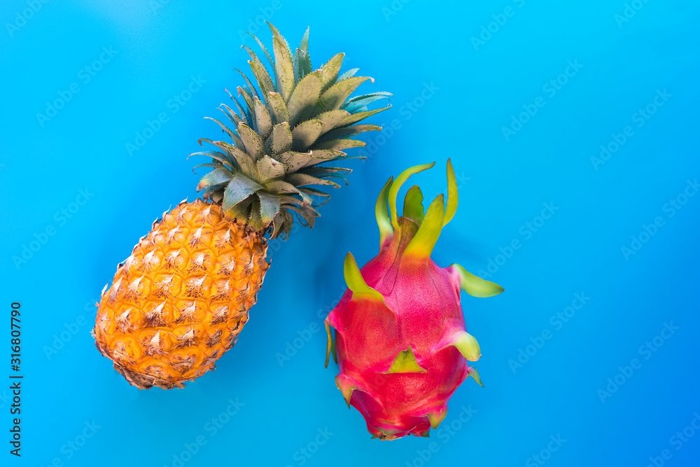 Fototapeta Exotic tropical colorful fruits on blue background. Fresh ripe yellow pineapple, ananas, red ripe dragon fruit, pitaya, cactus or pitahaya. Healthy vegan or vegetarian, vitamin food. Copy space.
