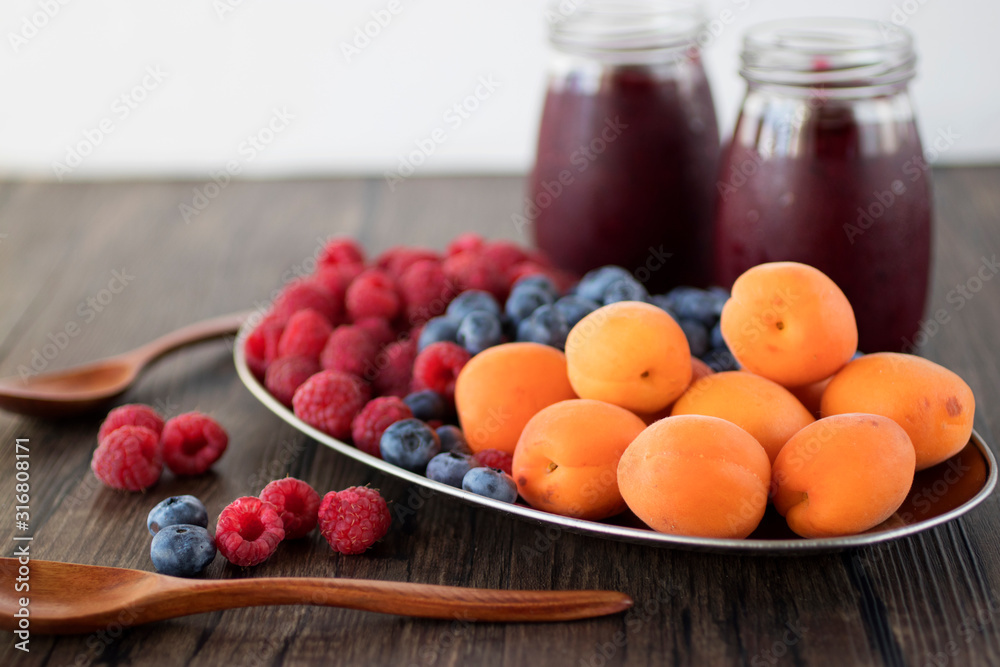 Fruit and berry smoothies and fresh apricots, raspberries and blueberries on an oval metal plate. Gray background. Fruit and berry smoothies and fresh apricots, raspberries and blueberries on an oval metal plate. Gray background.