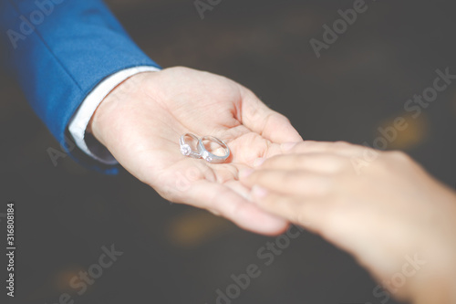 Close-up the Groom holding wedding rings on the palm and caressing hands of newlyweds