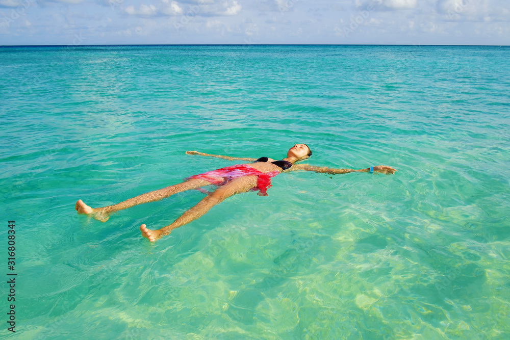 A girl swims on her back in the clear ocean on a sunny day