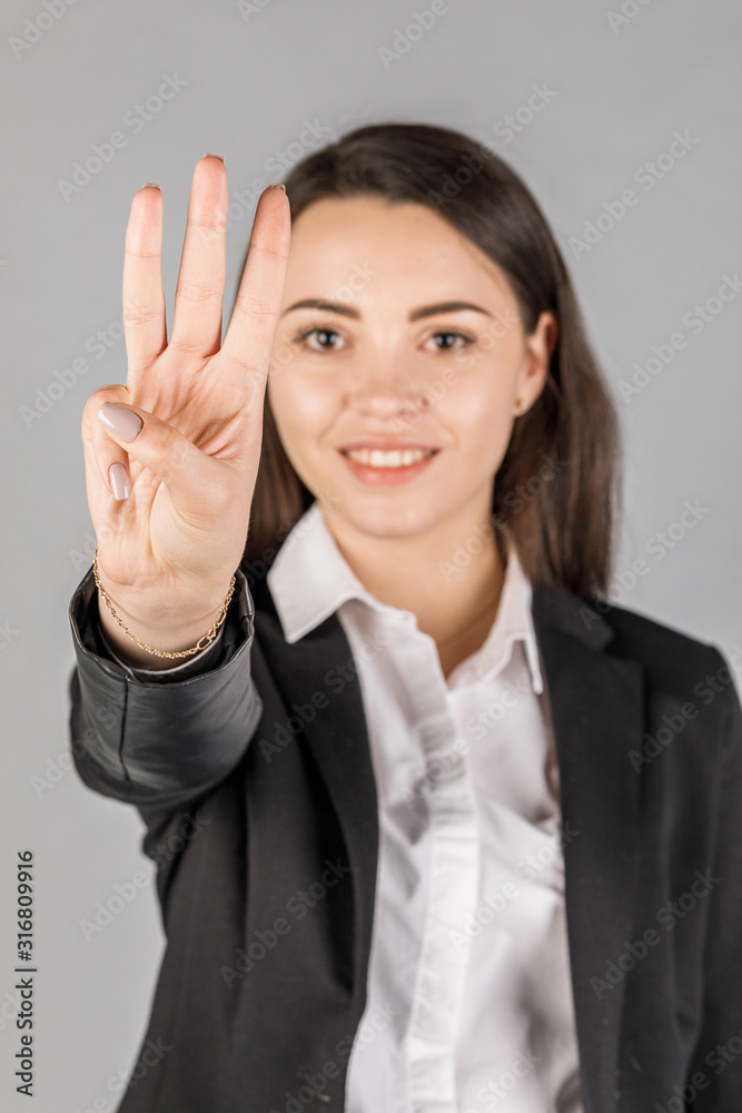 girl in black jacket on grey background showing 3 fingers girl in black jacket on grey background showing 3 fingers
